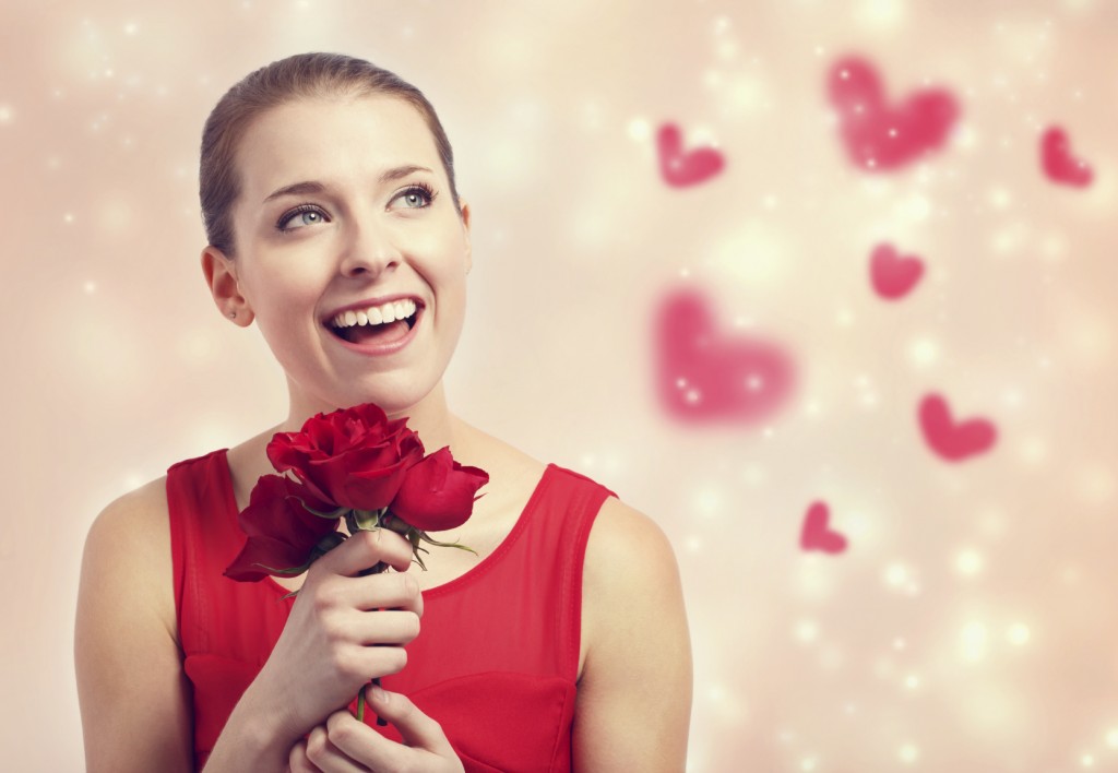 Happy young woman in red dress holding red roses